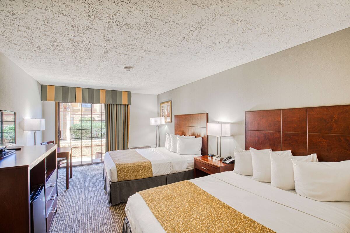 A hotel room with two beds, a desk, a chair, a nightstand, and a window with curtains.