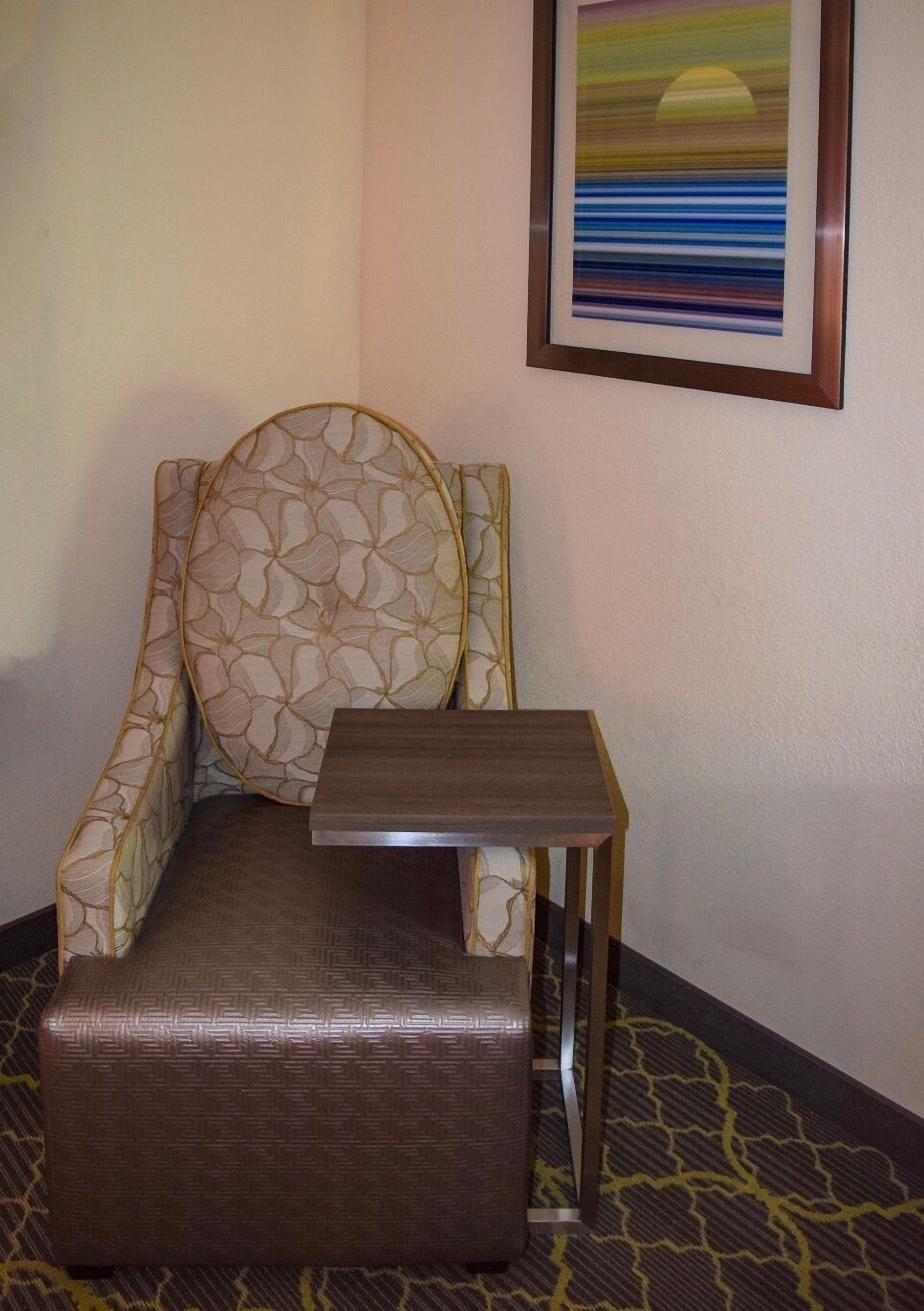A hotel room with a patterned armchair, a small wooden table, and a patterned carpet.