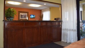 A reception area with a wooden reception desk, a potted plant, a framed picture, and a television screen.