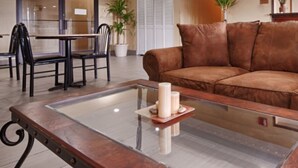 A living room with a brown leather sofa, a glass coffee table with candles, and a dining area with chairs and a table.