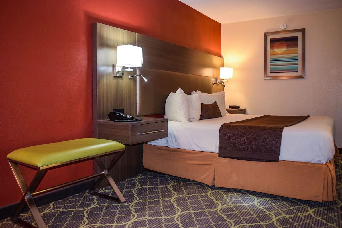 Ein Hotelzimmer mit einem Bett, einem Schreibtisch mit Lampe, einem Sessel und einem großen Spiegel.