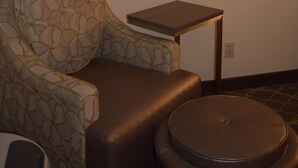 A hotel room with a sofa, a small table, and a painting of a landscape.