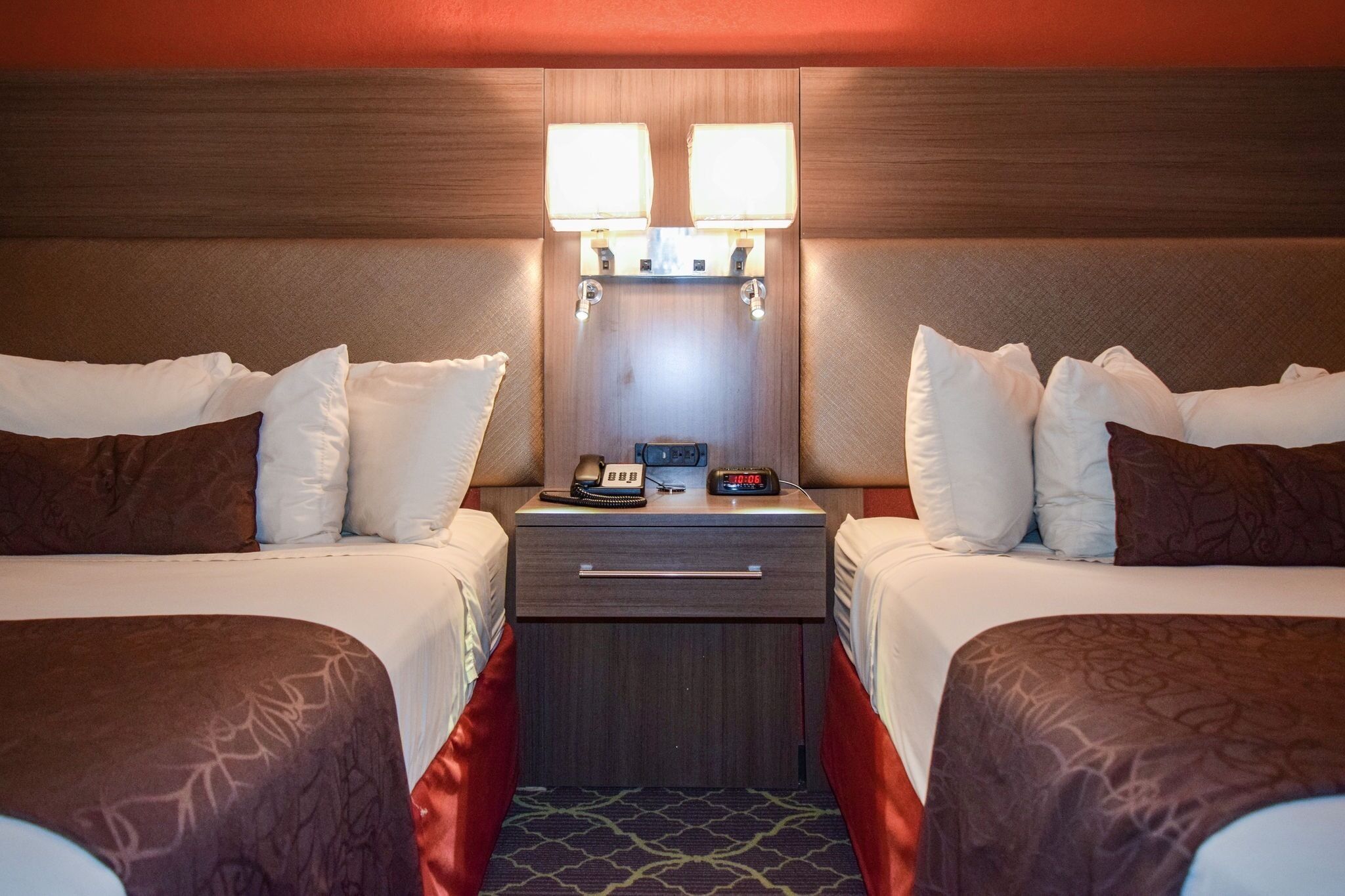Een hotelkamer met twee bedden, een nachtkastje met een klok en telefoon, en twee wandlampen.
