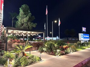 A well-lit outdoor area with a covered seating area, surrounded by landscaped gardens and a clear view of the sky.