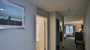 A hotel hallway with a framed picture, a door leading to a room, a seating area, and a window with curtains. - Best Western Surf City (Huntington Beach)