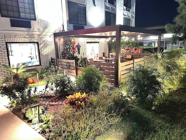 An outdoor seating area with a wooden fence, potted plants, and a brick wall in the background.