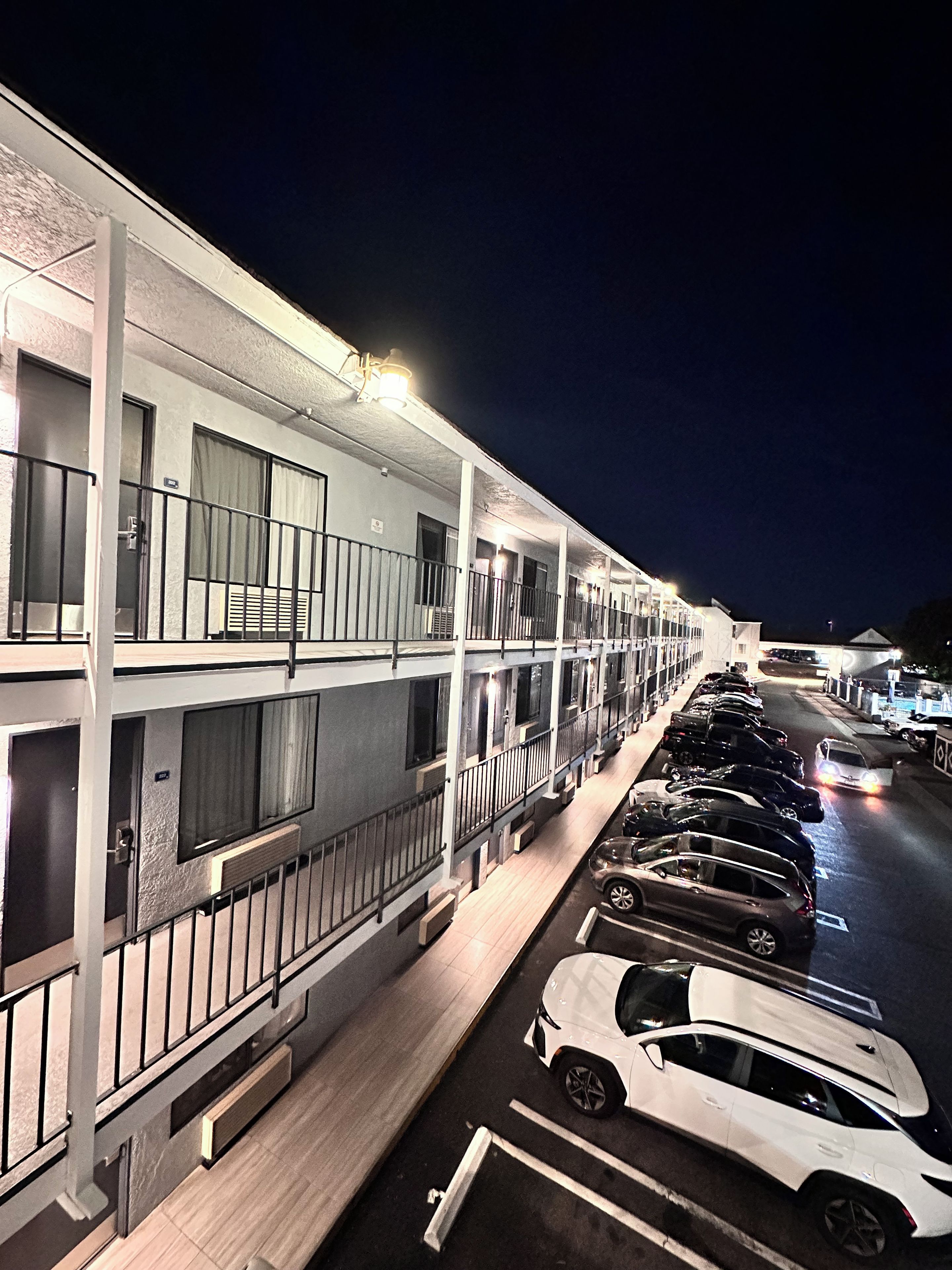 A multi-story motel with a row of parking spaces and a covered walkway.