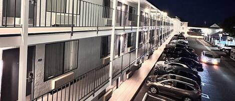 A multi-story motel with a row of parking spaces and a covered walkway.