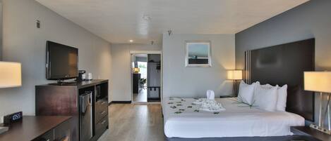 A hotel room with a bed, a desk, a television, and a view of the hallway.