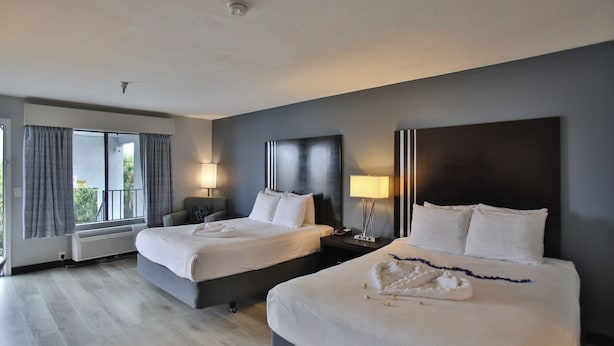 A hotel room with two beds, a large window with curtains, a ceiling light, and a bedside table with a lamp. - Best Western Surf City (Huntington Beach)