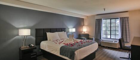 A hotel room with a large bed, bedside lamps, a desk, and a window with curtains.
