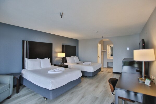 A hotel room with two beds, a desk, a chair, and a TV.