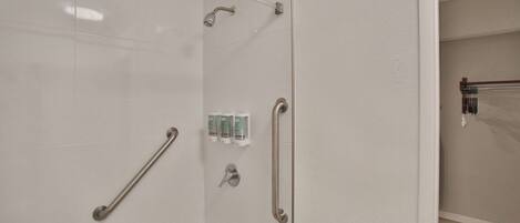 A bathroom with a glass shower enclosure, a handrail, and a towel rack.