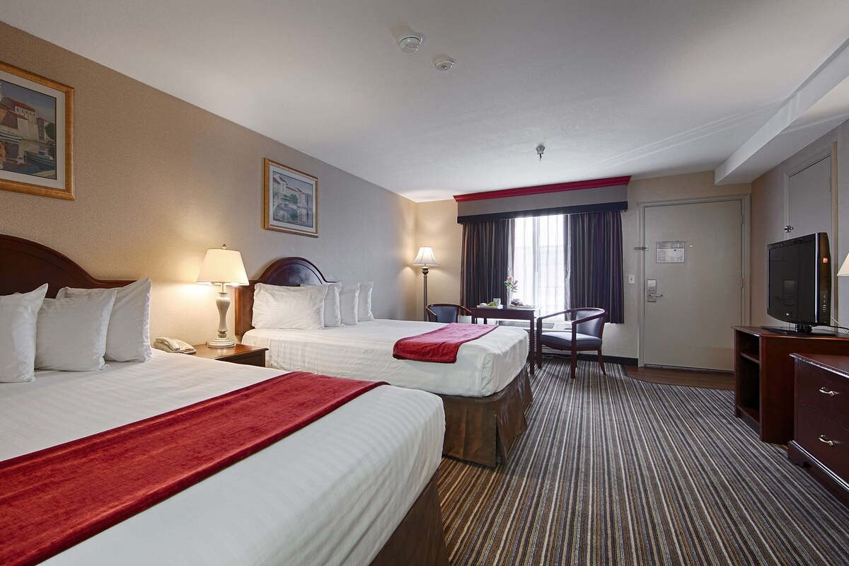 A hotel room with two beds, a desk, a chair, a television, and a window with curtains.
