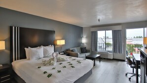 A hotel room with a large bed, a desk, a chair, a sofa, and a balcony with a view. - Best Western Surf City (Huntington Beach)