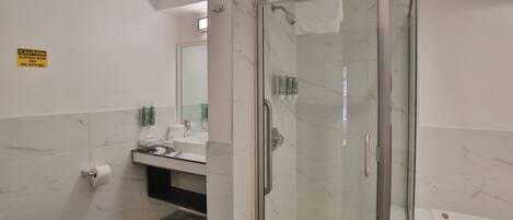 A bathroom with a glass-enclosed shower, a toilet, a sink with a mirror, and a caution sign on the wall.