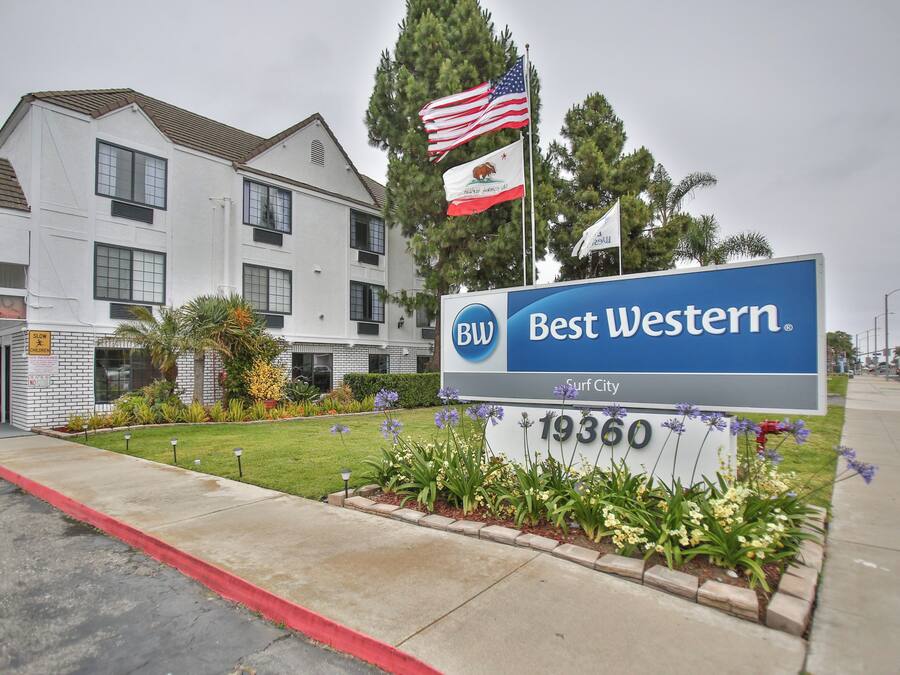 Une enseigne d’hôtel Best Western avec l’adresse 19360, entourée d’un jardin aménagé avec des fleurs et d’un mât sur lequel flottent deux drapeaux.