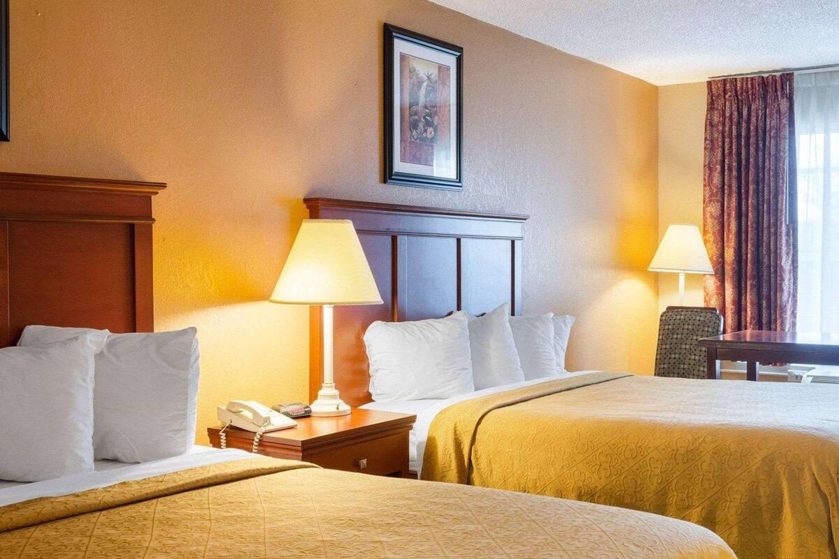 A hotel room with two beds, a desk, a chair, a telephone, and a framed picture on the wall.