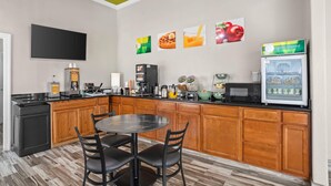 A kitchen with a black countertop, wooden cabinets, a black dining table with four chairs, a microwave, a coffee maker, and a refrigerator. - Quality Inn Louisville MS (Louisville)