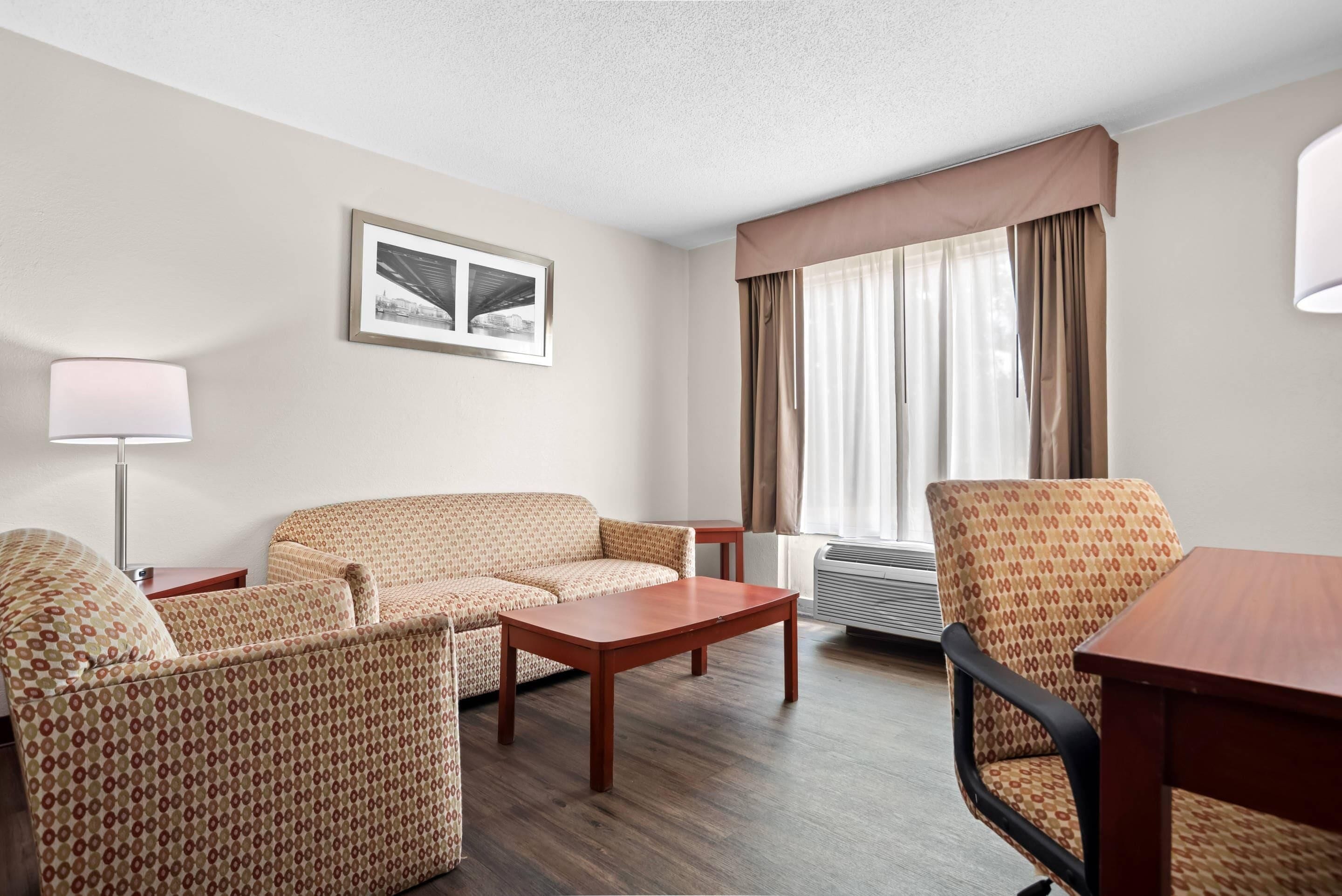 A hotel room with a sofa, armchair, wooden coffee table, and a framed picture on the wall.