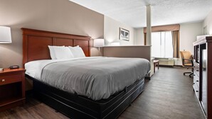 A hotel room with a bed, bedside table, lamp, chair, desk, and television. - Quality Inn Louisville MS (Louisville)