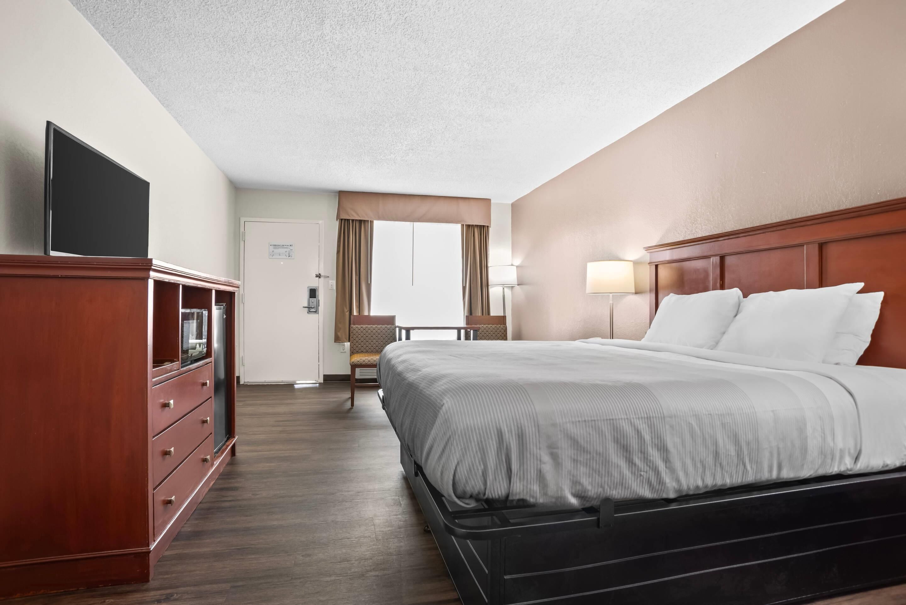 A hotel room with a bed, a dresser, a television, a desk, and a mirror.