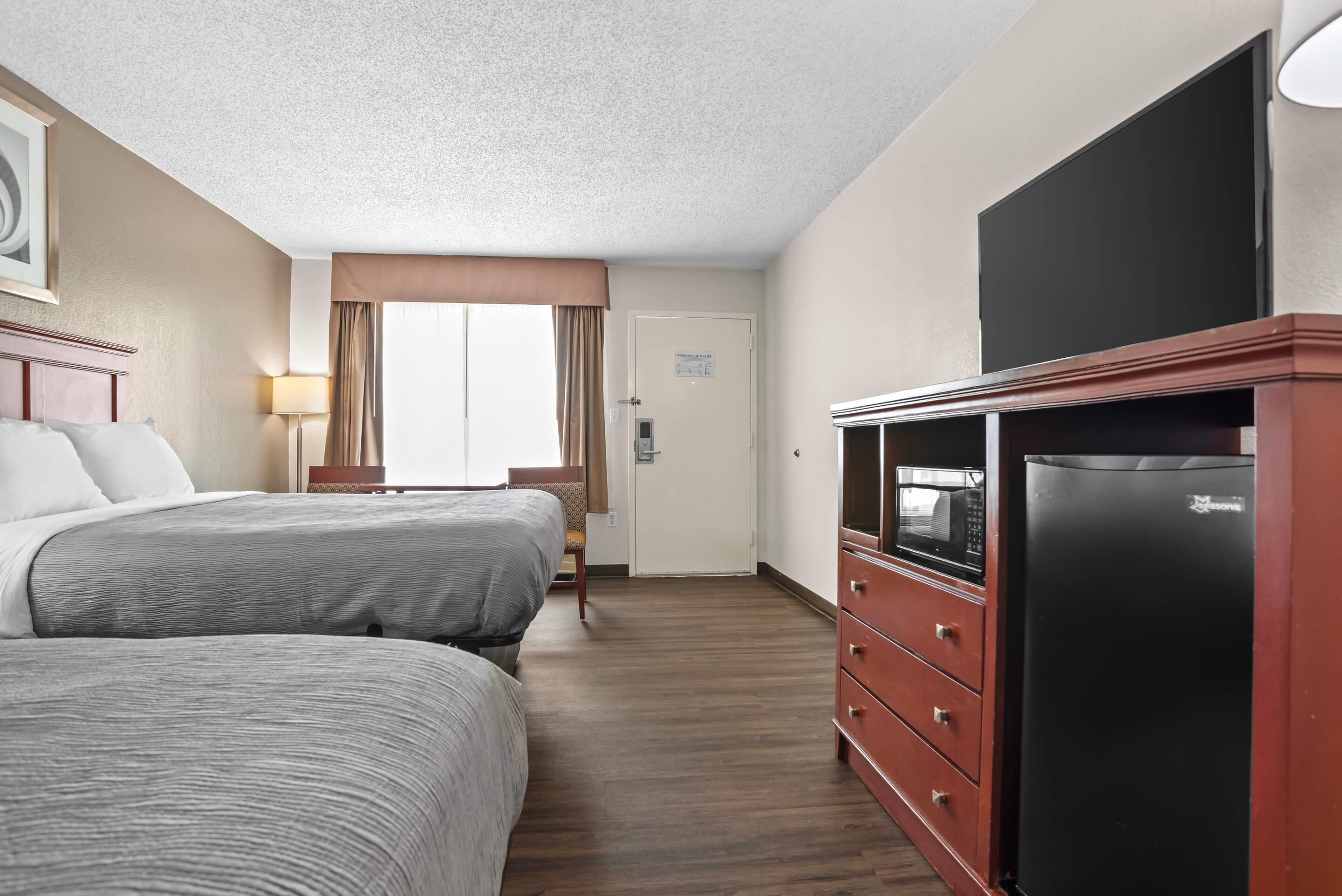 A hotel room with two beds, a TV, a refrigerator, and a door with a sign.