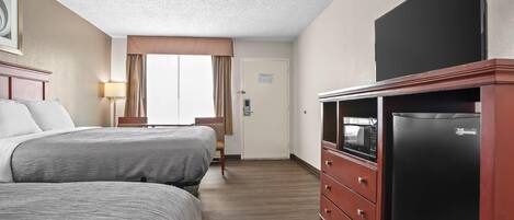 A hotel room with two beds, a TV, a refrigerator, and a door with a sign.