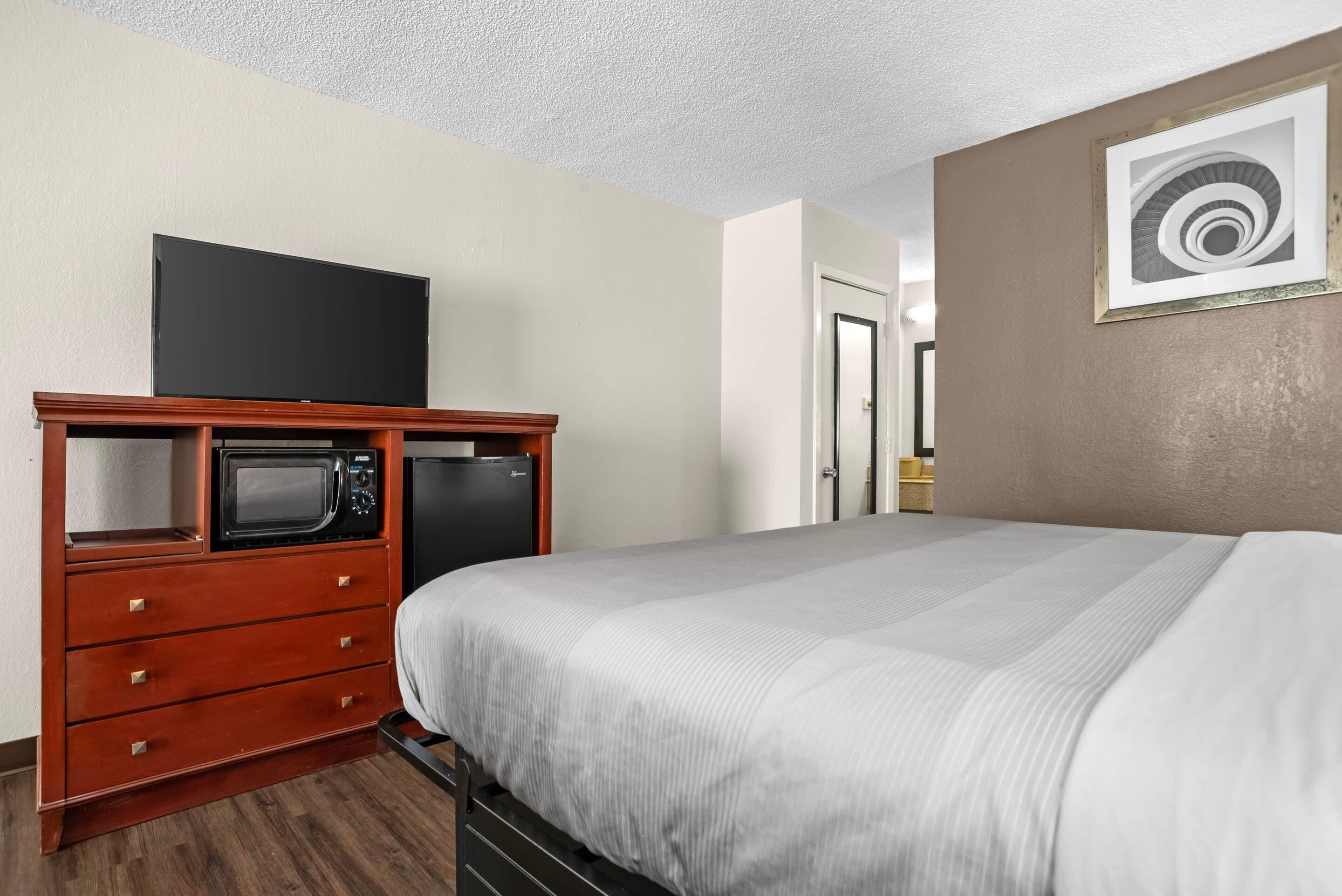 Een hotelkamer met een bed, een houten dressoir met een magnetron, een televisie en een deur naar een badkamer.