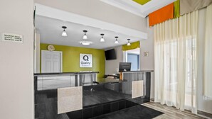 A reception area with a clock, a sign indicating breakfast hours, a television, and a reception desk. - Quality Inn Louisville MS (Louisville)