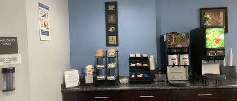 Una estación de café con una máquina de café, un dispensador de agua y un panel con el menú.