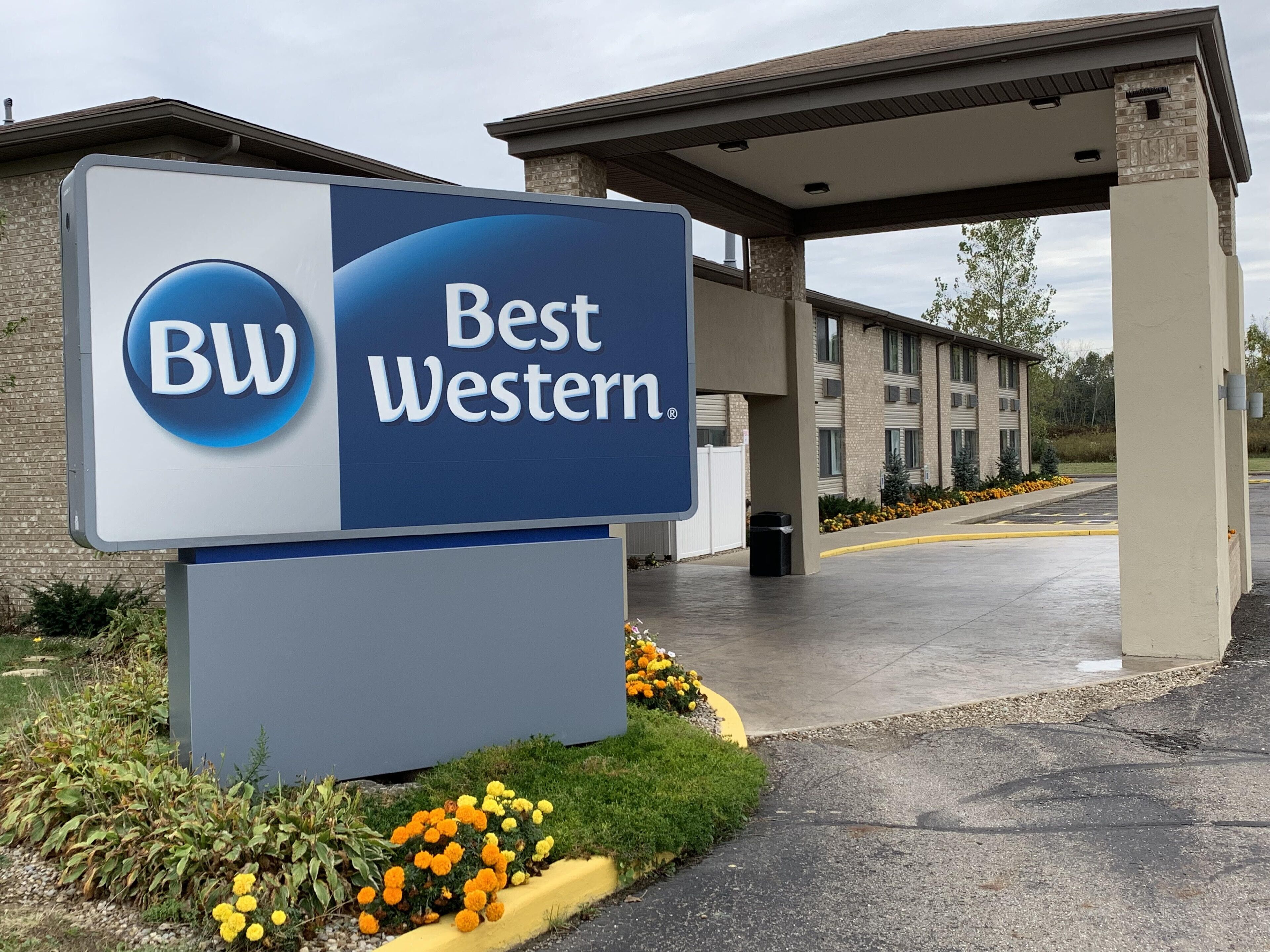 A Best Western sign with a blue and white logo, a building with a covered entrance, and a parking lot with yellow lines.