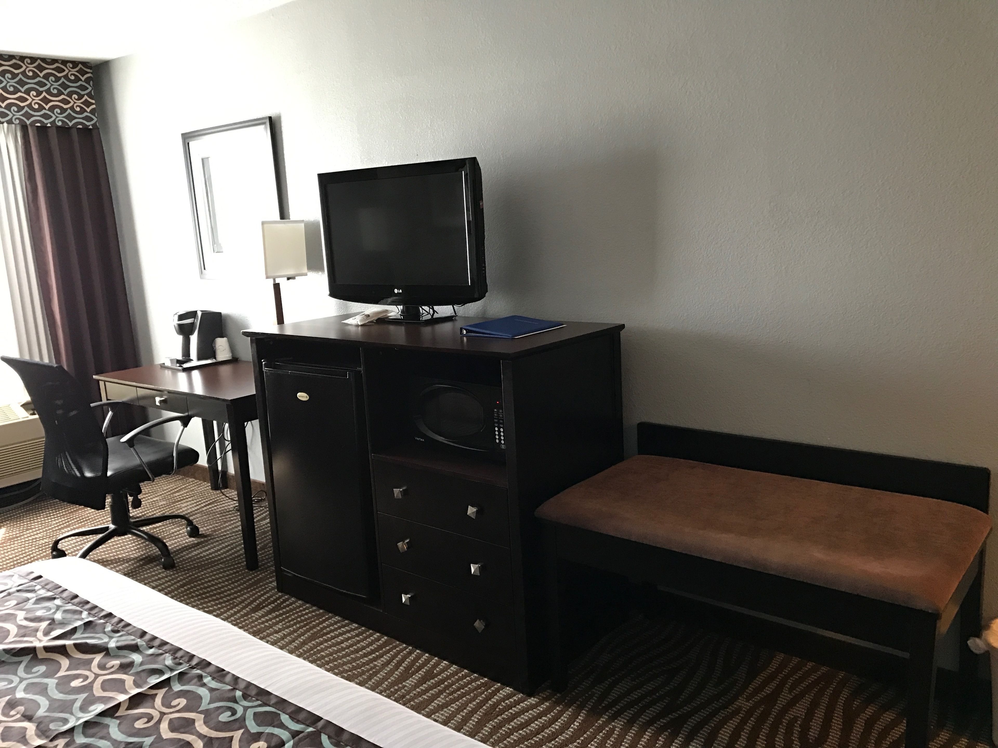 A hotel room with a bed, a desk with a computer, a television, and a microwave.