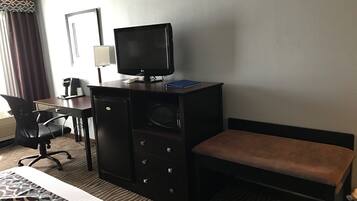 A hotel room with a bed, a desk with a computer, a television, and a microwave.