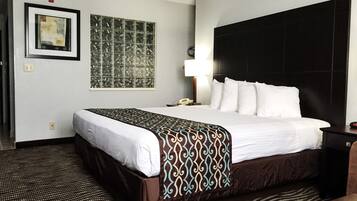 Habitación de hotel con una cama grande, cabecera, mesita de noche, lámpara y una obra de arte en la pared.