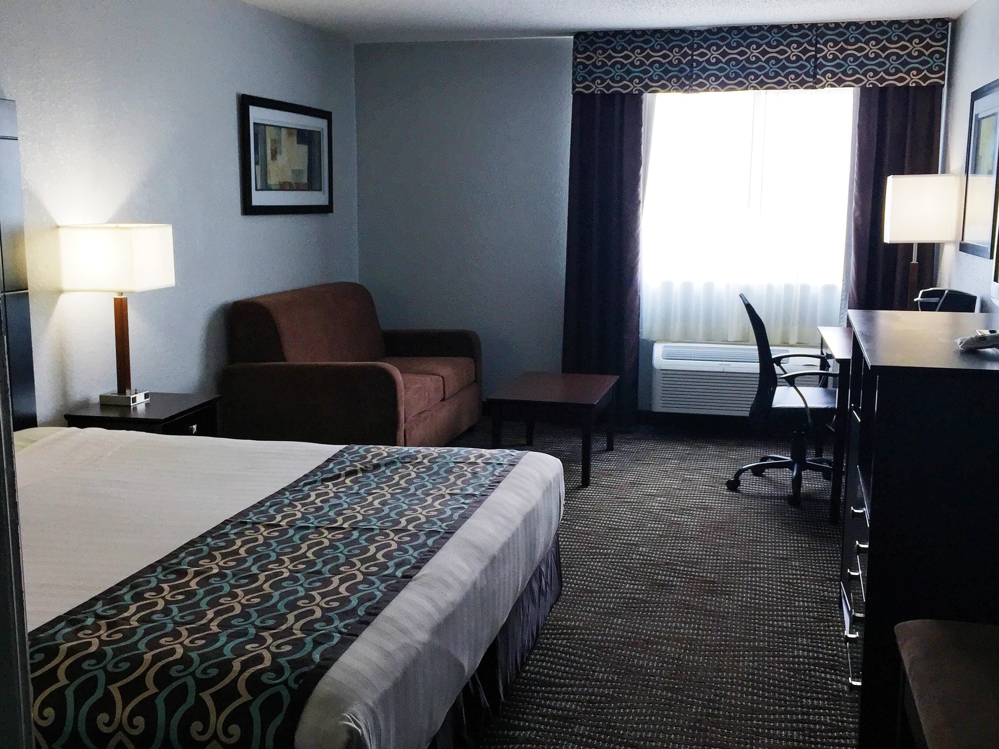 A hotel room with a bed, a desk, a chair, a lamp, and a window with curtains.