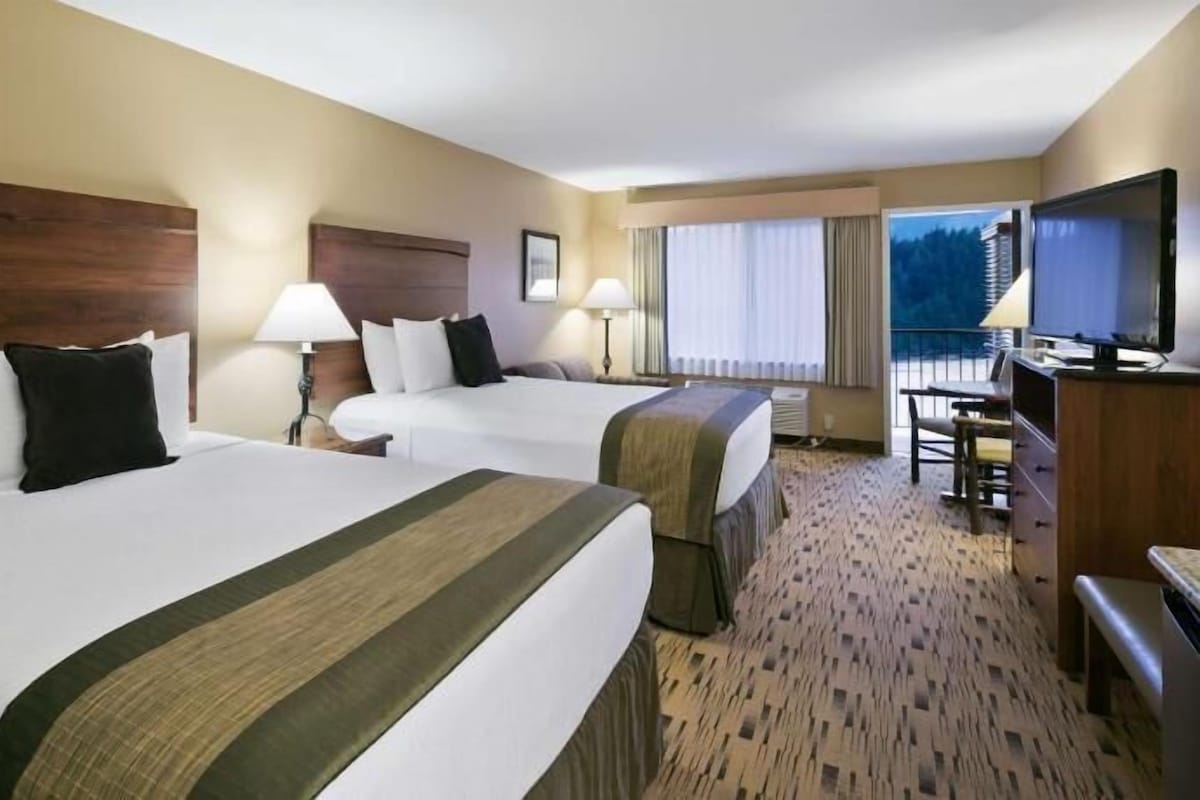 Habitación de hotel con dos camas, televisor, escritorio y ventana con cortinas.