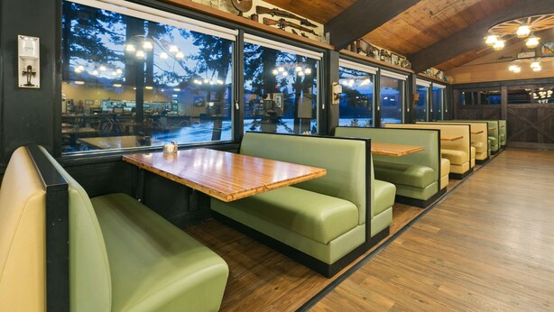 A restaurant with green booths and wooden tables, large windows with a view of trees and a snowy landscape. - Best Western Plus Columbia River Inn (Cascade Locks)