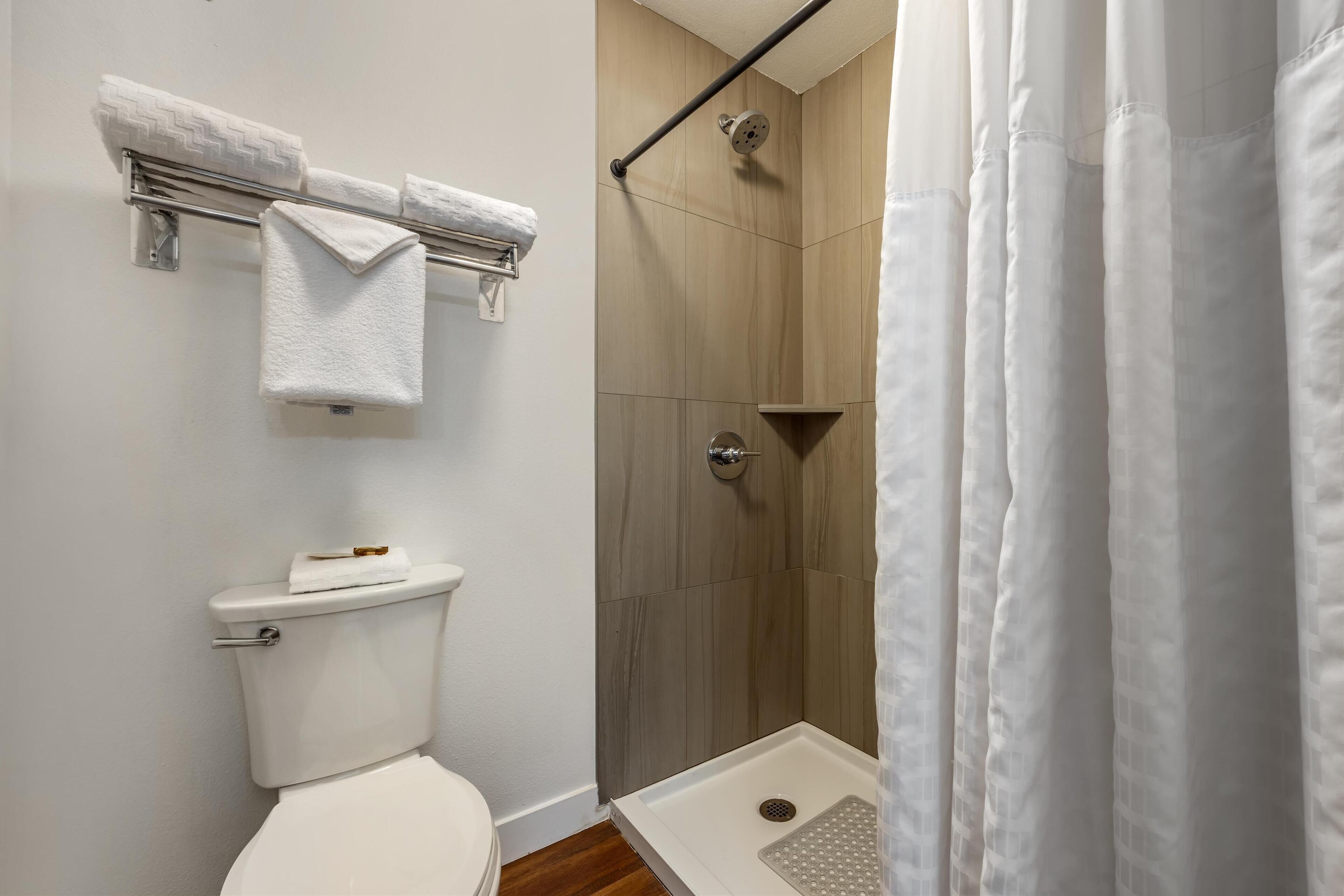 Ein Badezimmer mit einer weißen Toilette, einer Dusche mit Glastür und einem Handtuchhalter mit zwei Handtüchern.