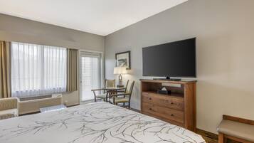 Quarto de hotel com uma cama grande, televisão, escrivaninha com cadeira e janela com cortinas.