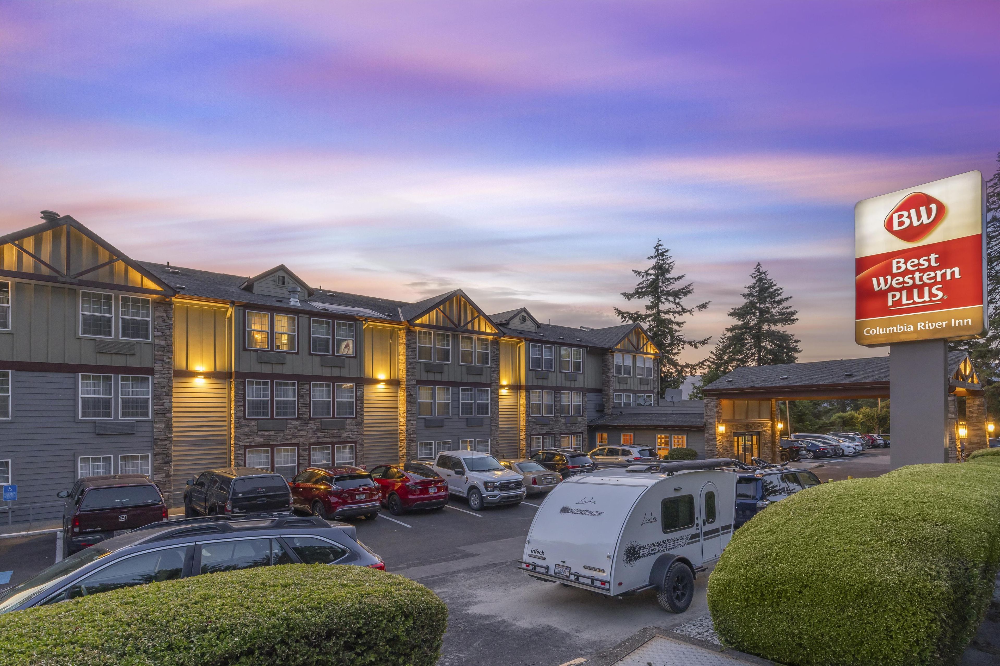 Un hotel Best Western Plus con varios espacios de estacionamiento, una caravana y una fachada de edificio bien iluminada.