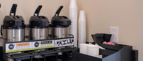 A coffee station with three coffee makers, disposable cups, and a trash bin.