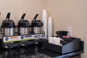 Una estación de café con tres máquinas de café, vasos desechables y un cubo de basura.