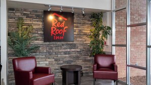 Une enseigne « Red Roof Inn » sur un mur de pierre, deux fauteuils en cuir, une petite table et des plantes en pot.