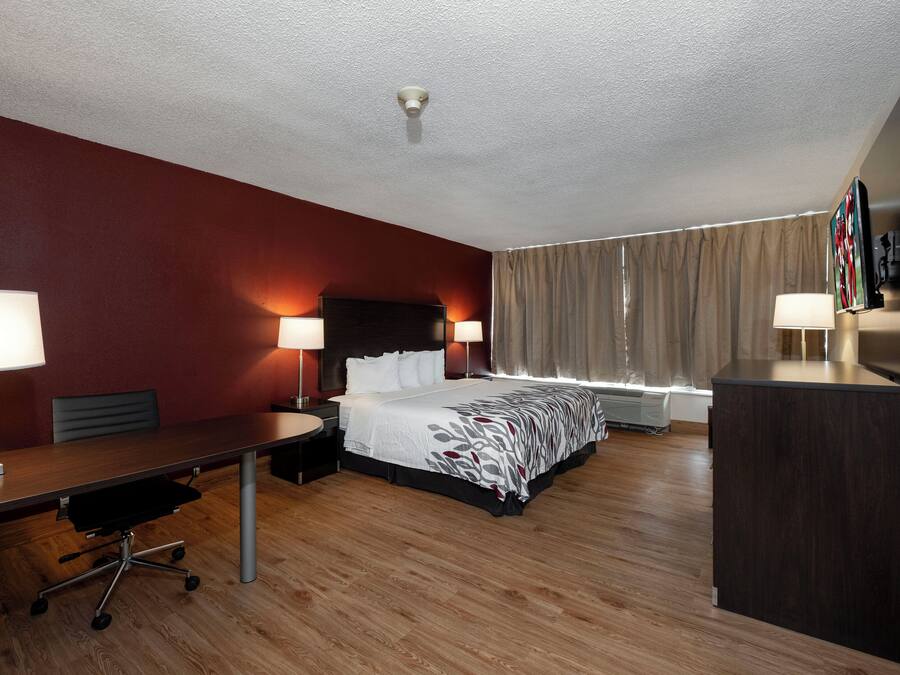 A hotel room with a bed, desk, chair, lamps, curtains, and a television.