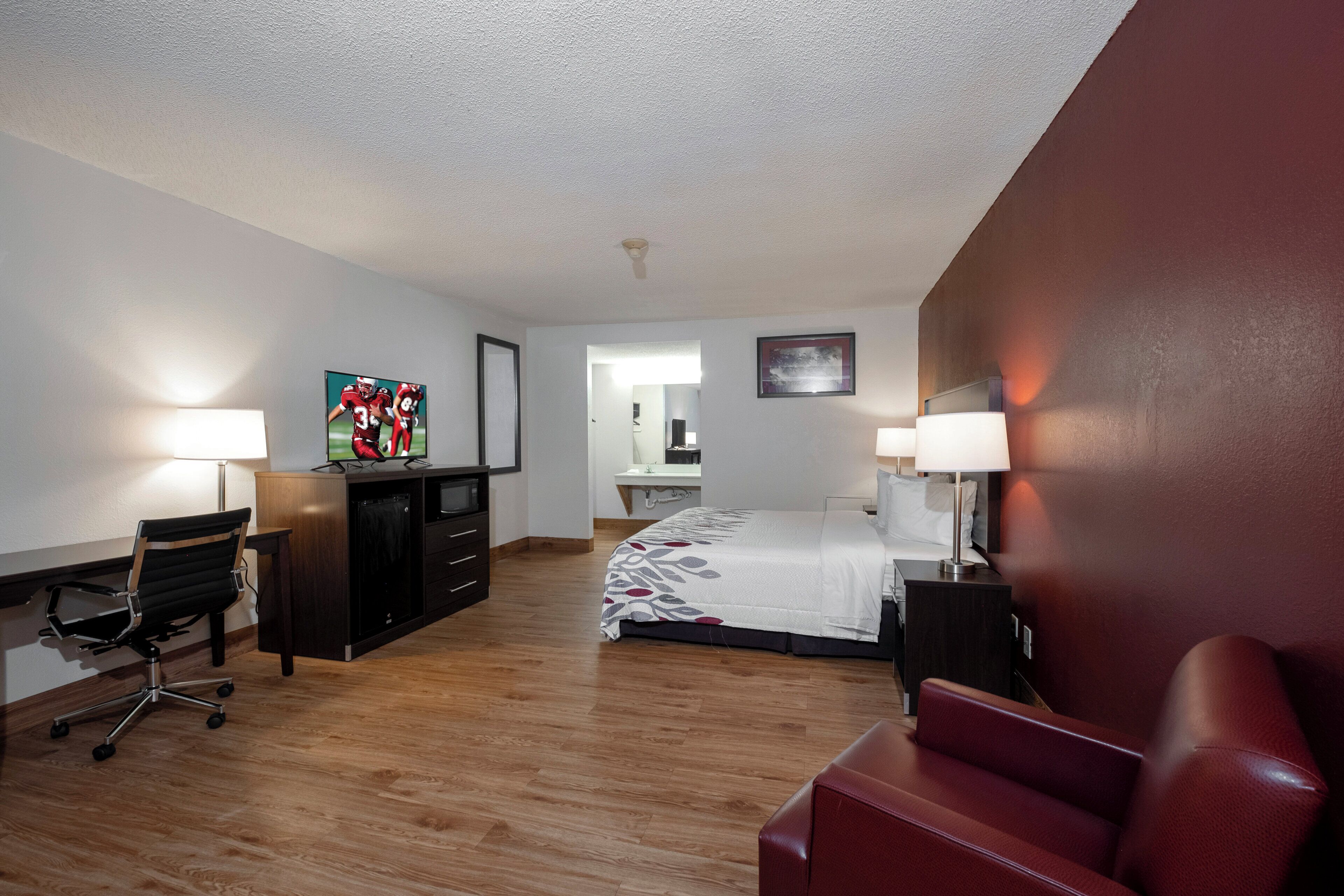 A hotel room with a bed, desk, chair, and a red sofa.