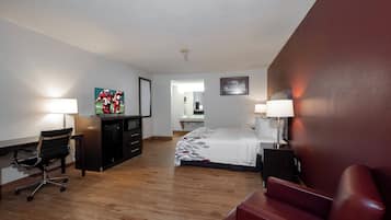 A hotel room with a bed, desk, chair, and a red sofa.