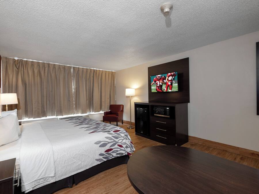 Een hotelkamer met een bed, een aan de muur bevestigde televisie, een bureau, een stoel en een houten vloer.