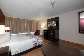 Ett hotellrum med en säng, en tv som är monterad på väggen, ett skrivbord, en stol och ett trägolv.