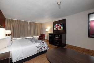 Habitación de hotel con cama, televisión montada en la pared, escritorio, silla y suelo de madera.